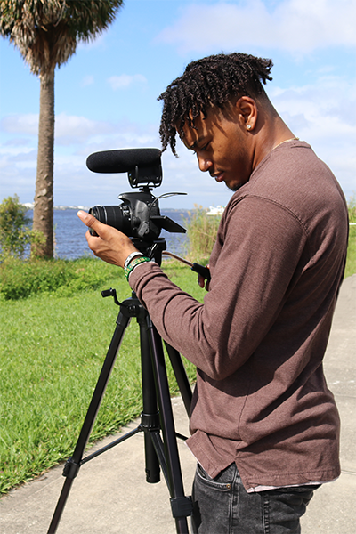 Male student filming on the river with a camera on a tripod.