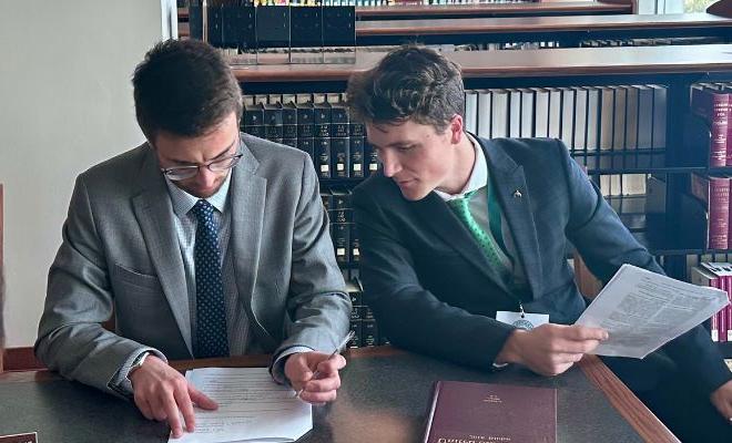 Two male students sharing a book in a legal library.