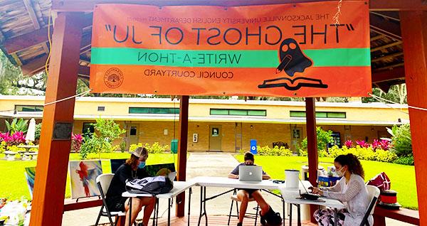 Students sitting outside under a gazebo writing on laptops while socially-distanced for 