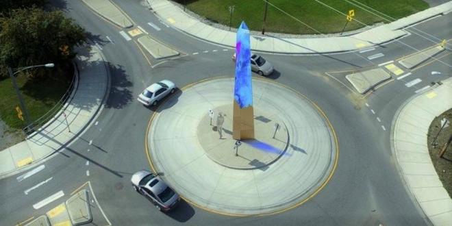 a roundabout with three cars going around, and an art sculpture in the middle in blue