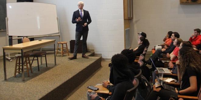 male teacher speaking emotively in front of a classroom of students