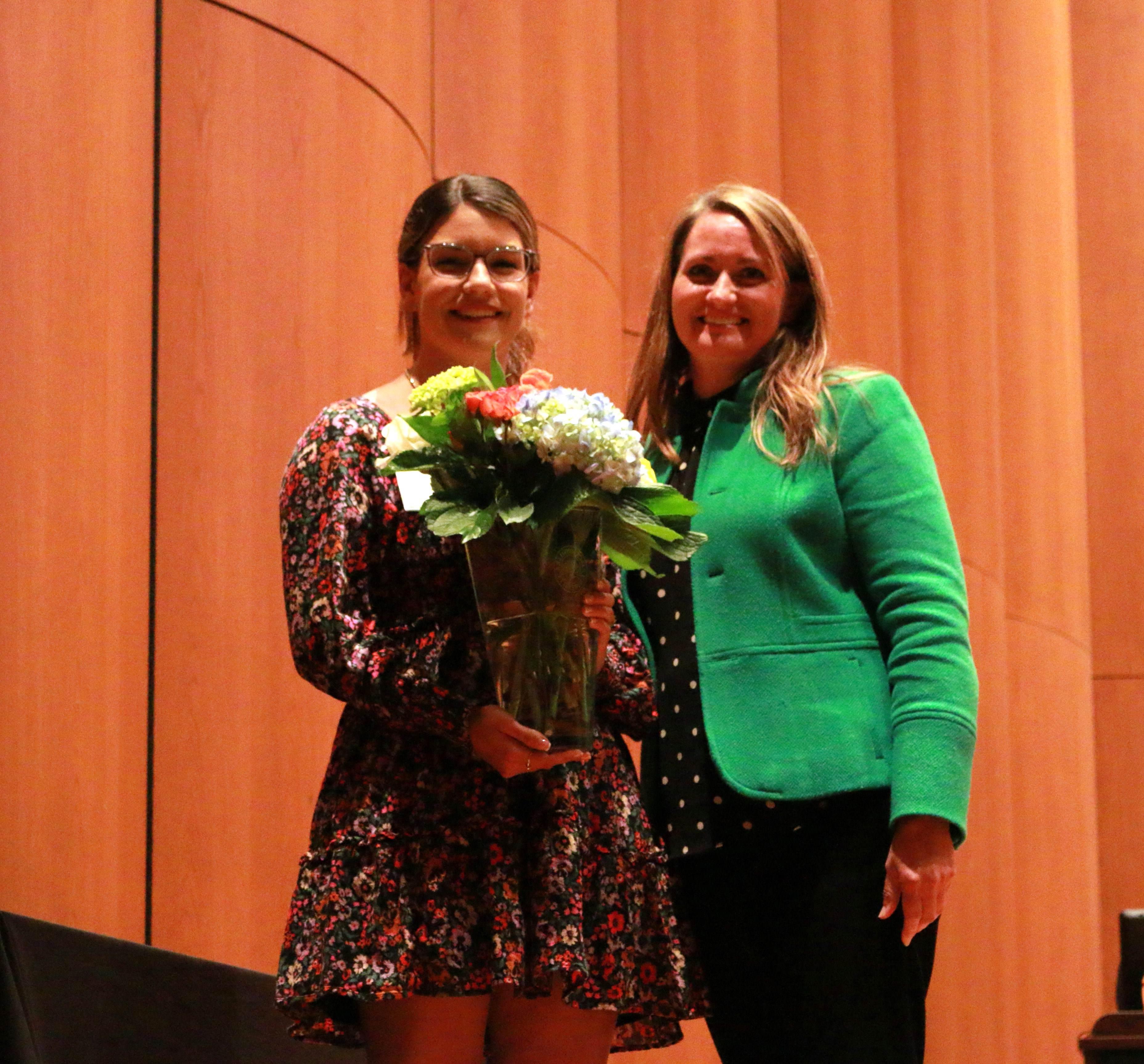 Two women standing beside eachother, one holding a vase of flowers