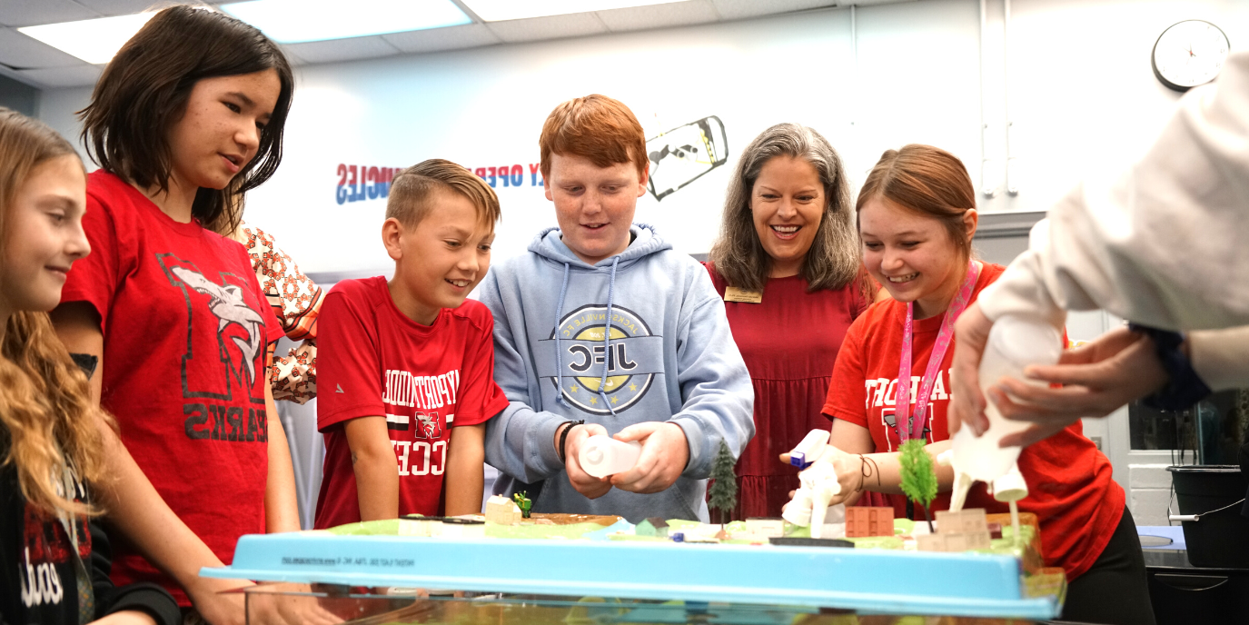 Students are smiling at an educational model surrounding one teacher