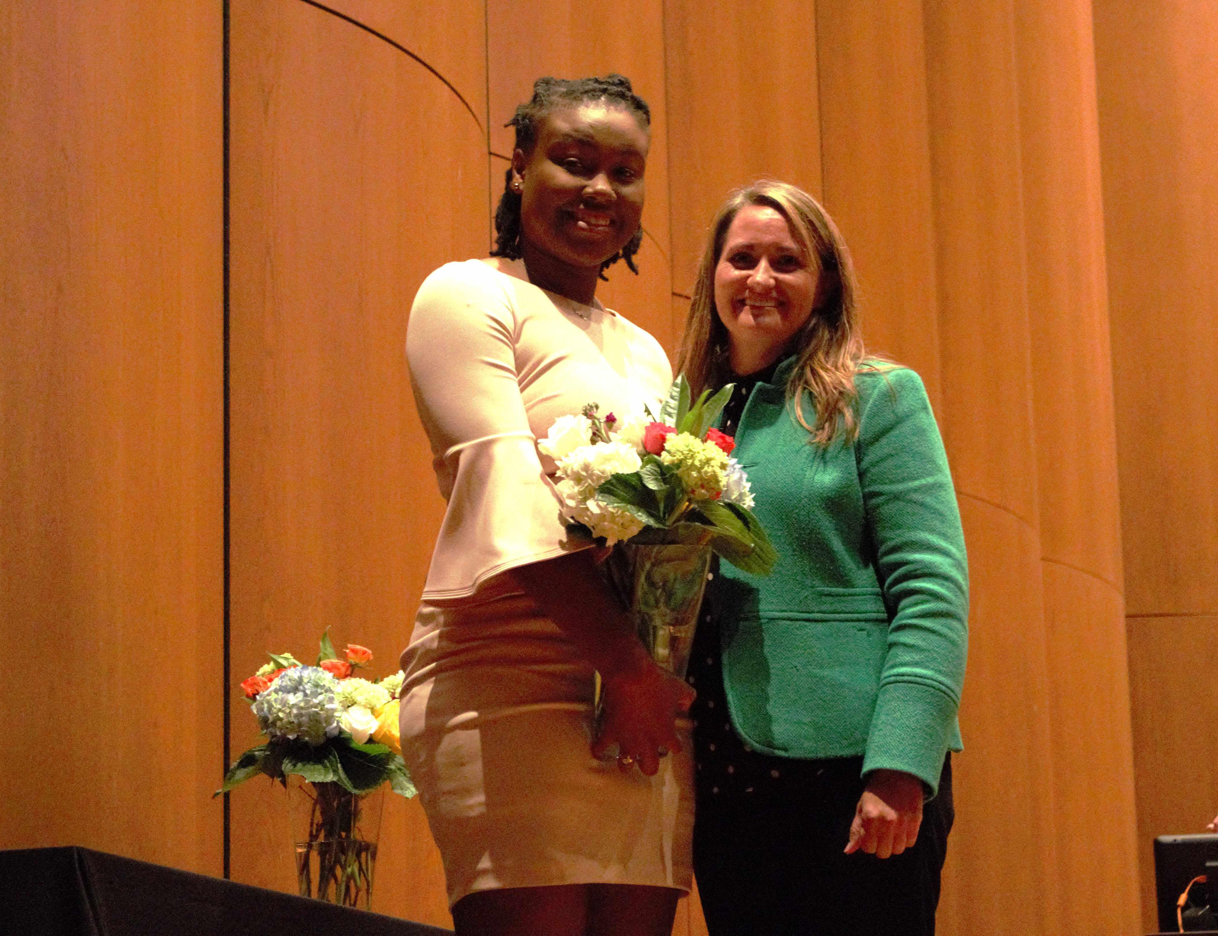 Two women standing beside eachother, one holding a vase of flowers