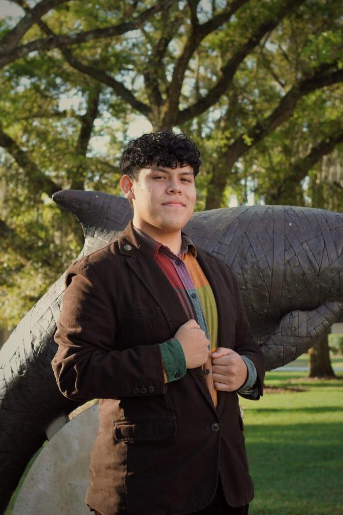 Sophomore student Bradley Cordero standing in front of a dolphin statue