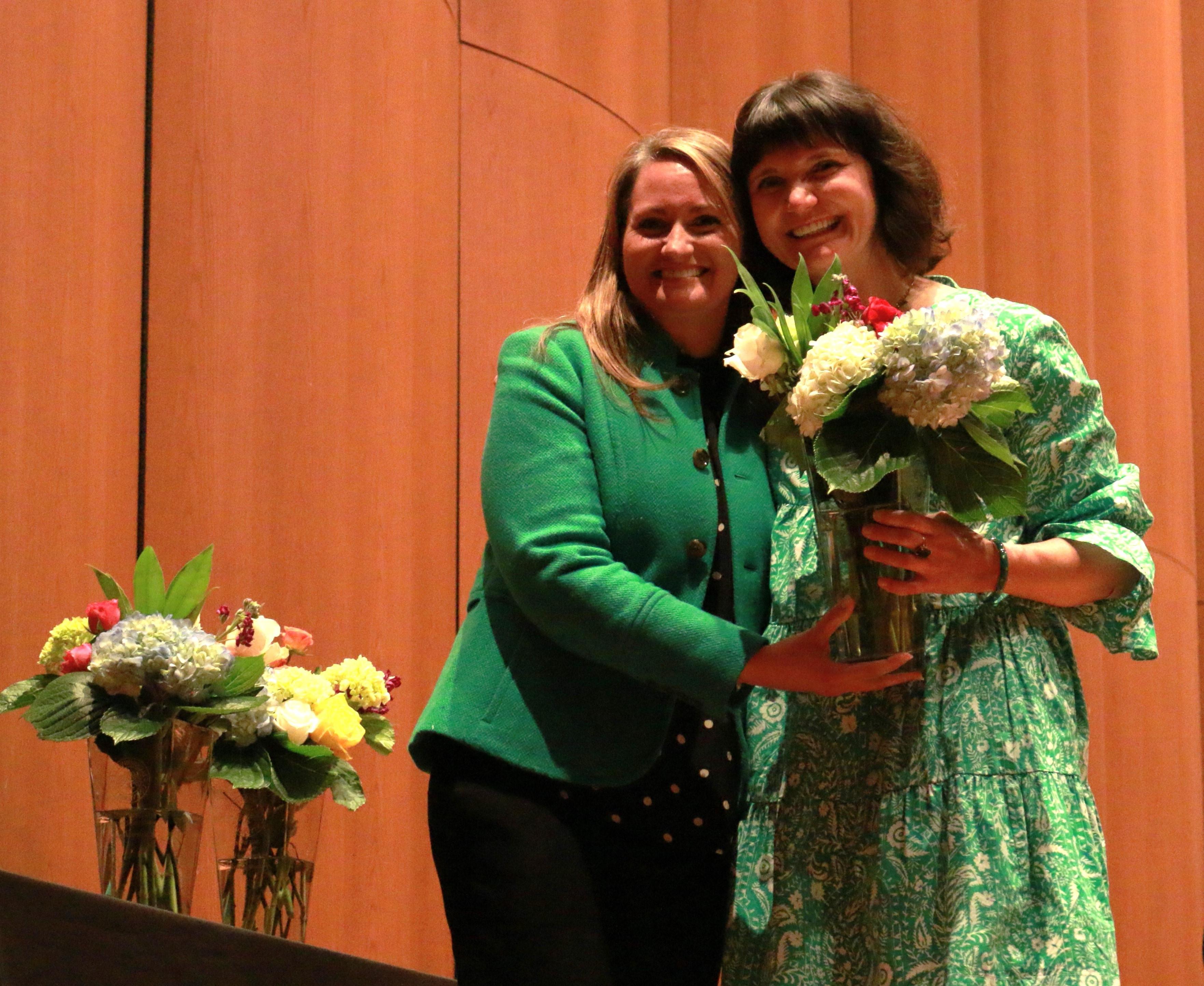 Two women standing beside eachother, one holding a vase of flowers