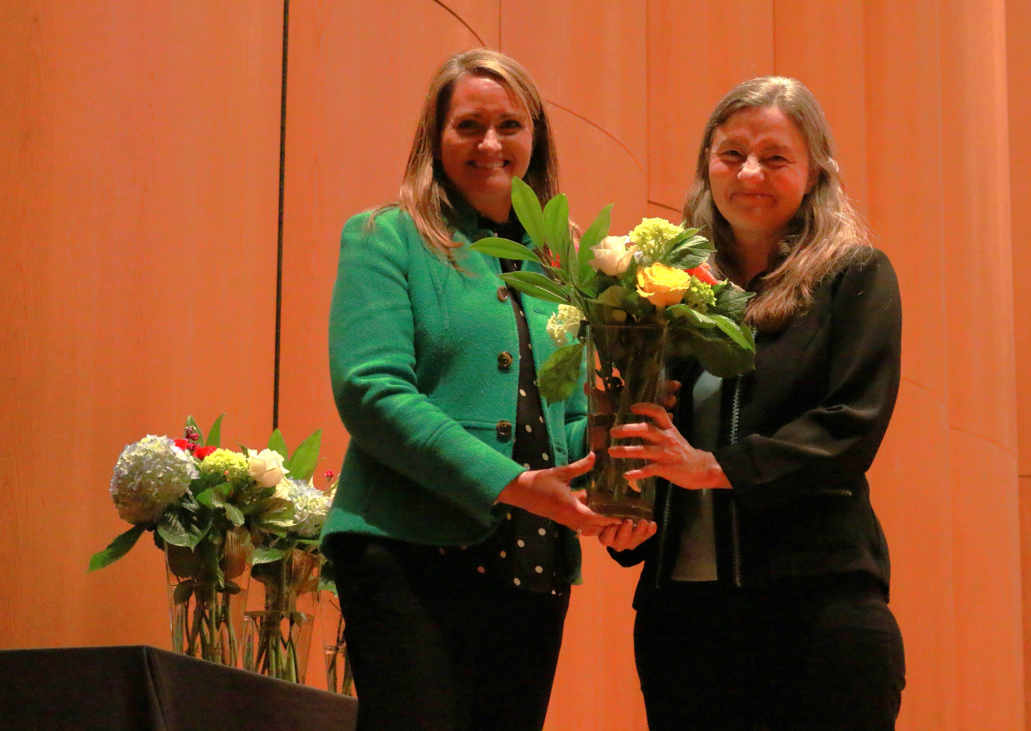 Two women standing beside eachother, one holding a vase of flowers