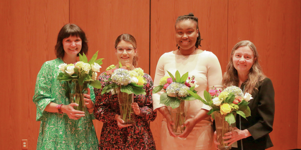 four women standing shoulder to shoulder holding vases of flowers, honored as women of the year in their respective categories