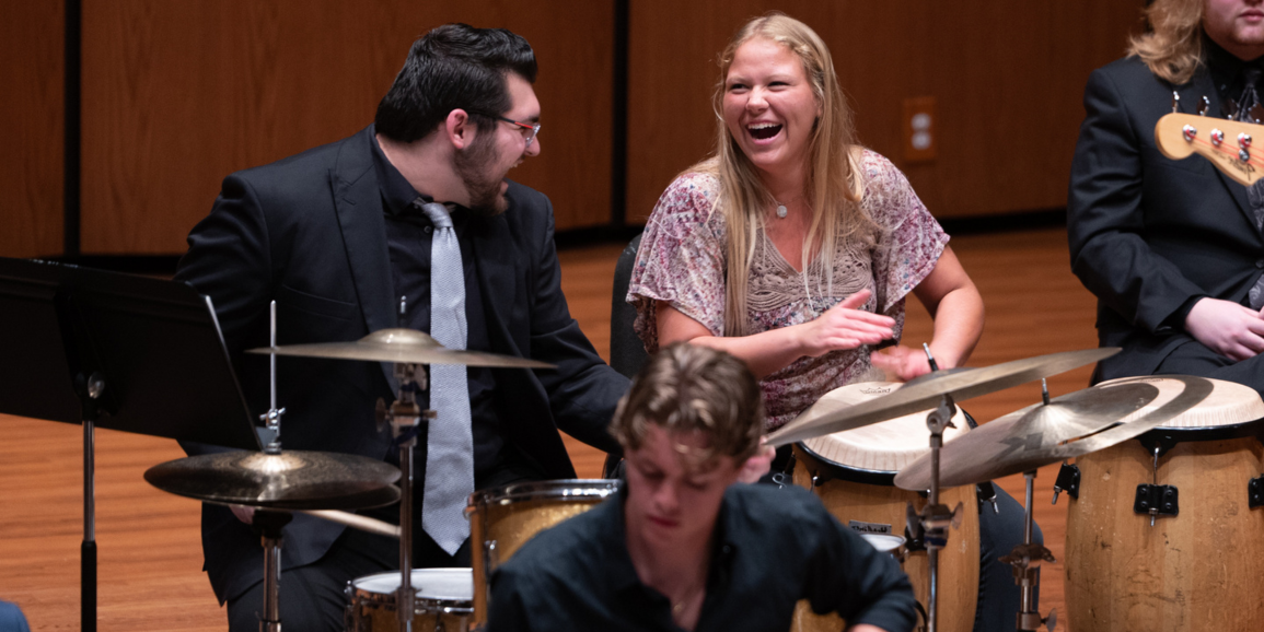 two nicely dressed students laughing at each other while playing instruments on stage